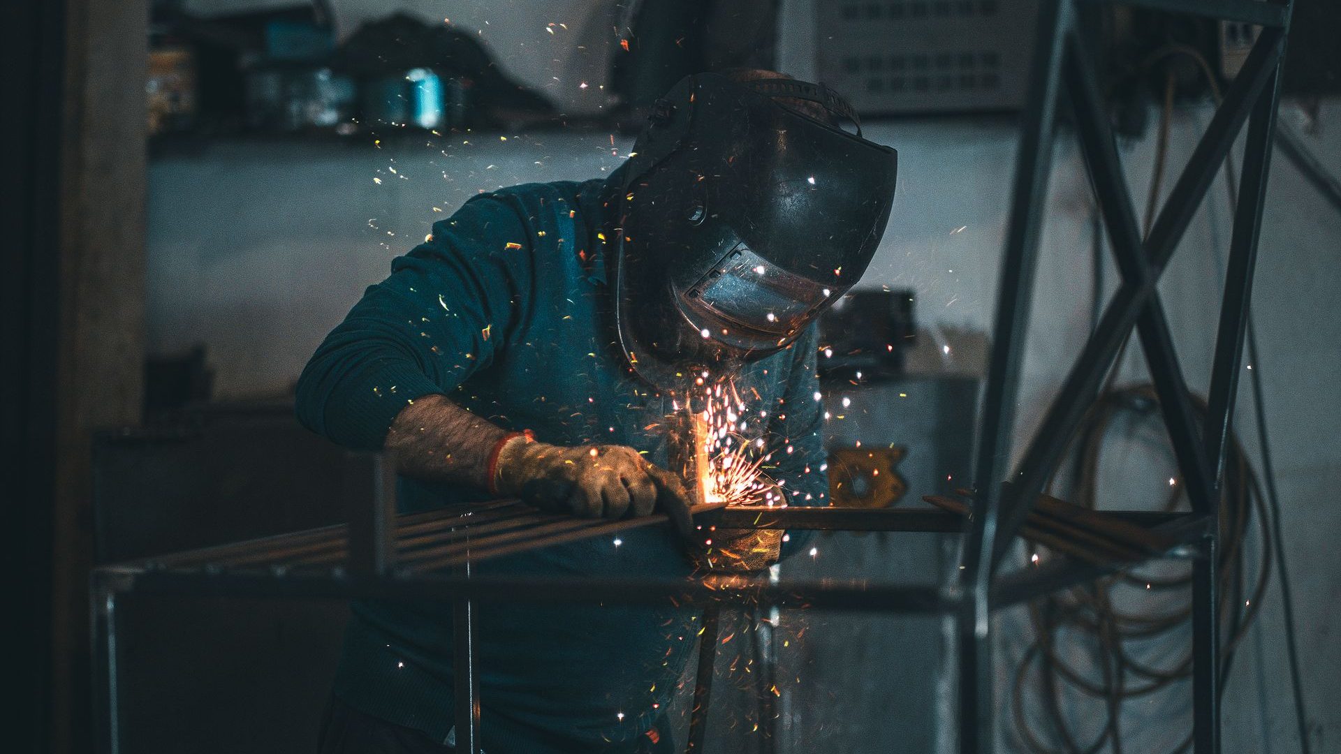Metallbauer schweißt in der Werkstatt an einem Stahlrahmen, Funken sprühen